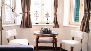 A cozy room with a round wooden table, two white upholstered chairs, a blue sofa, and a floor lamp. - Hotel Vila Katrca (Ljubljana)