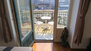 A balcony with a table and chairs, a statue, and a view of a street with buildings and parked cars. - Hotel Vila Katrca (Ljubljana)