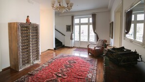 A spacious room with a large wooden cabinet, a patterned rug, a chair, and a vintage suitcase. - Hotel Vila Katrca (Ljubljana)