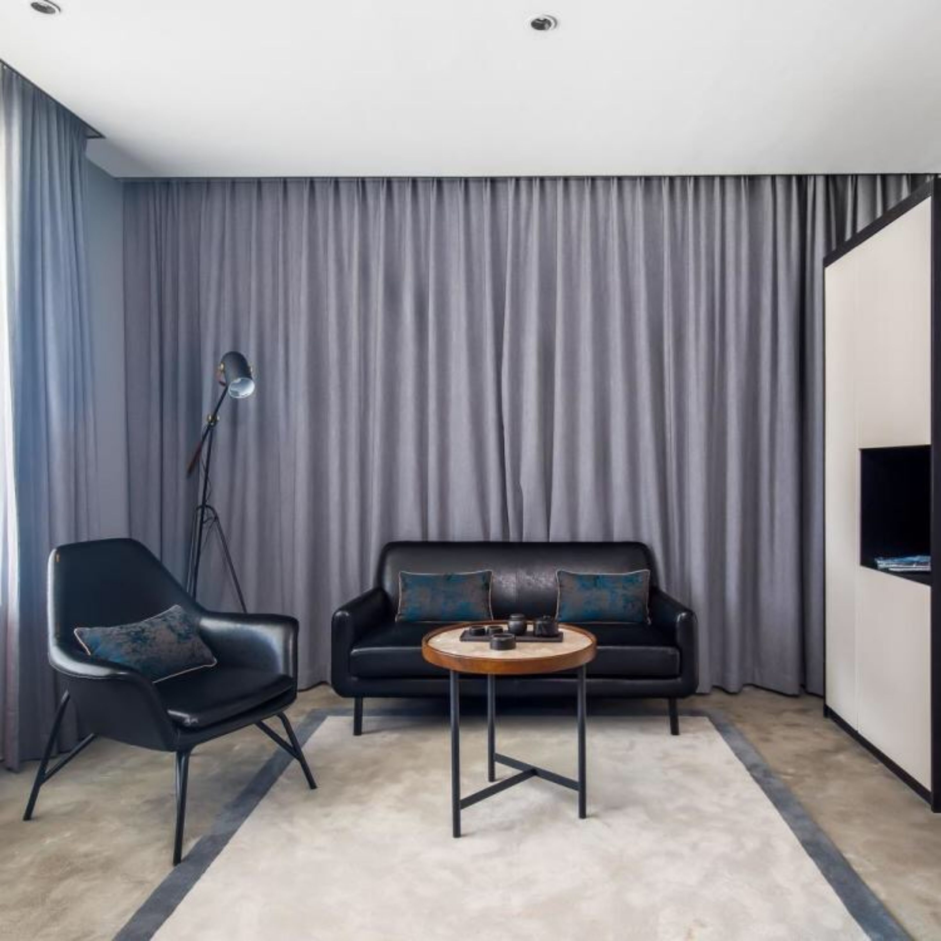A modern living room with a black leather sofa, a round coffee table, and a black armchair.