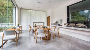 Un comedor moderno con mesas y sillas redondas, un ventanal con cortinas y una encimera de cocina con electrodomésticos.