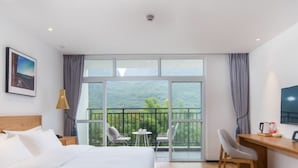 A hotel room with a bed, a desk, a chair, and a balcony with a view of greenery. - Floral Hotel Yangshuo Xiatangzhai (Guilin)