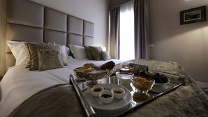Una habitación de hotel con una cama bien hecha, una bandeja con alimentos para el desayuno y una ventana con cortinas.