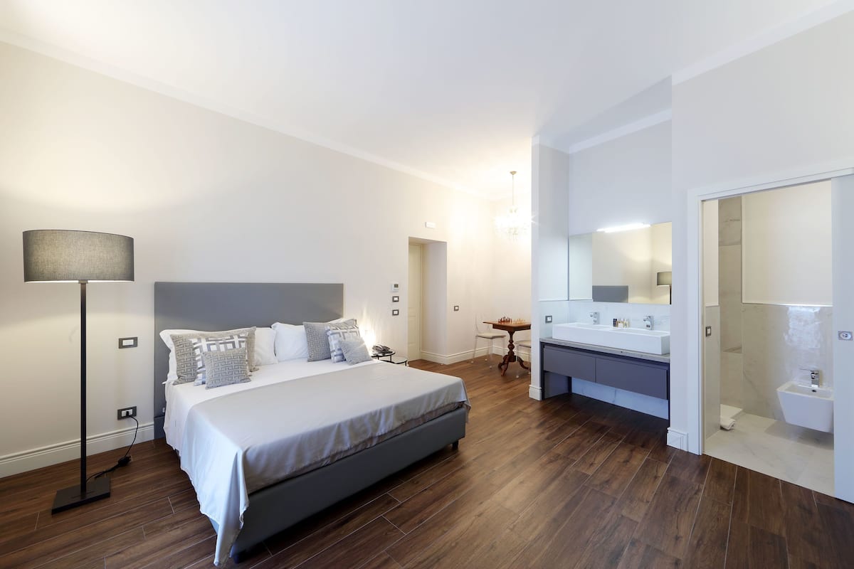 A modern bedroom with a large bed, bedside table, and a bathroom with a sink and mirror.