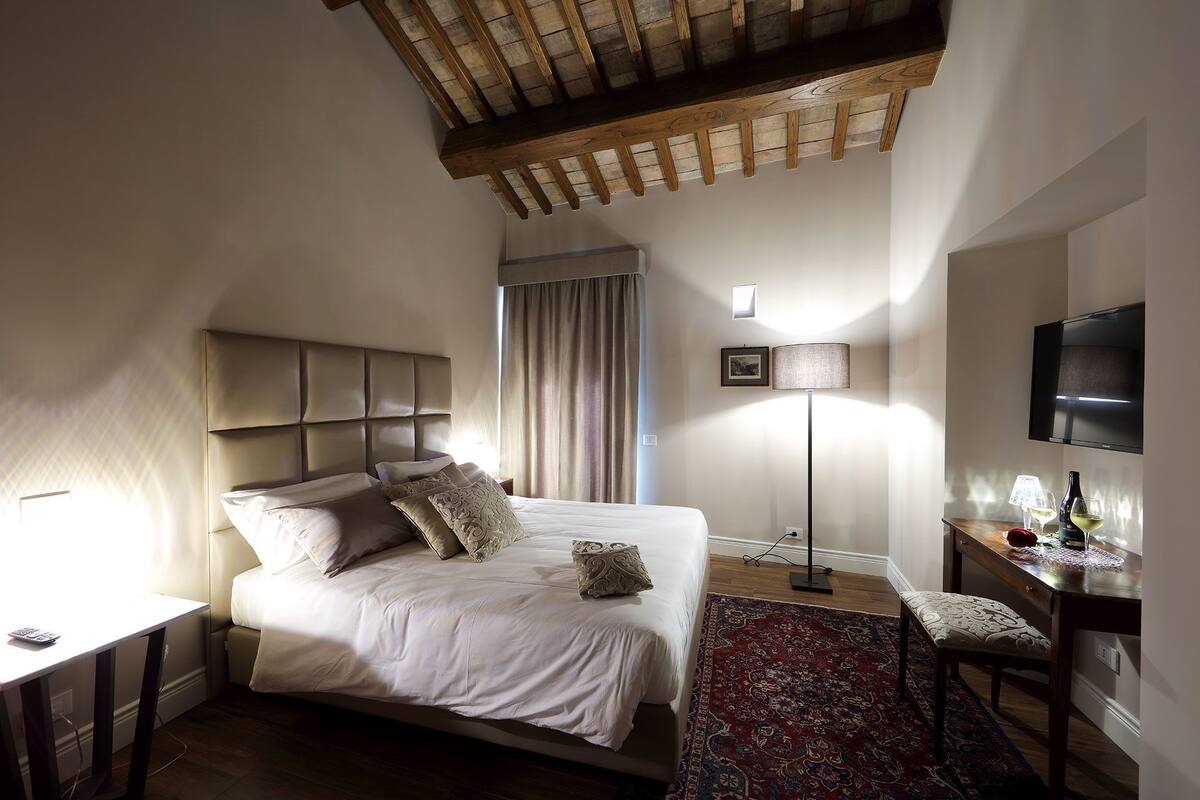 A bedroom with a large bed, a desk, a chair, a TV, and a floor lamp.