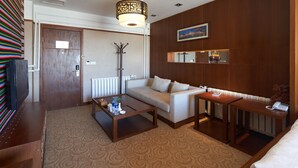 A modern hotel room with a sofa, a coffee table, a small table with a phone, a radiator, and a painting on the wall. - Floral Hotel Shangri-la Budange (Deqin)