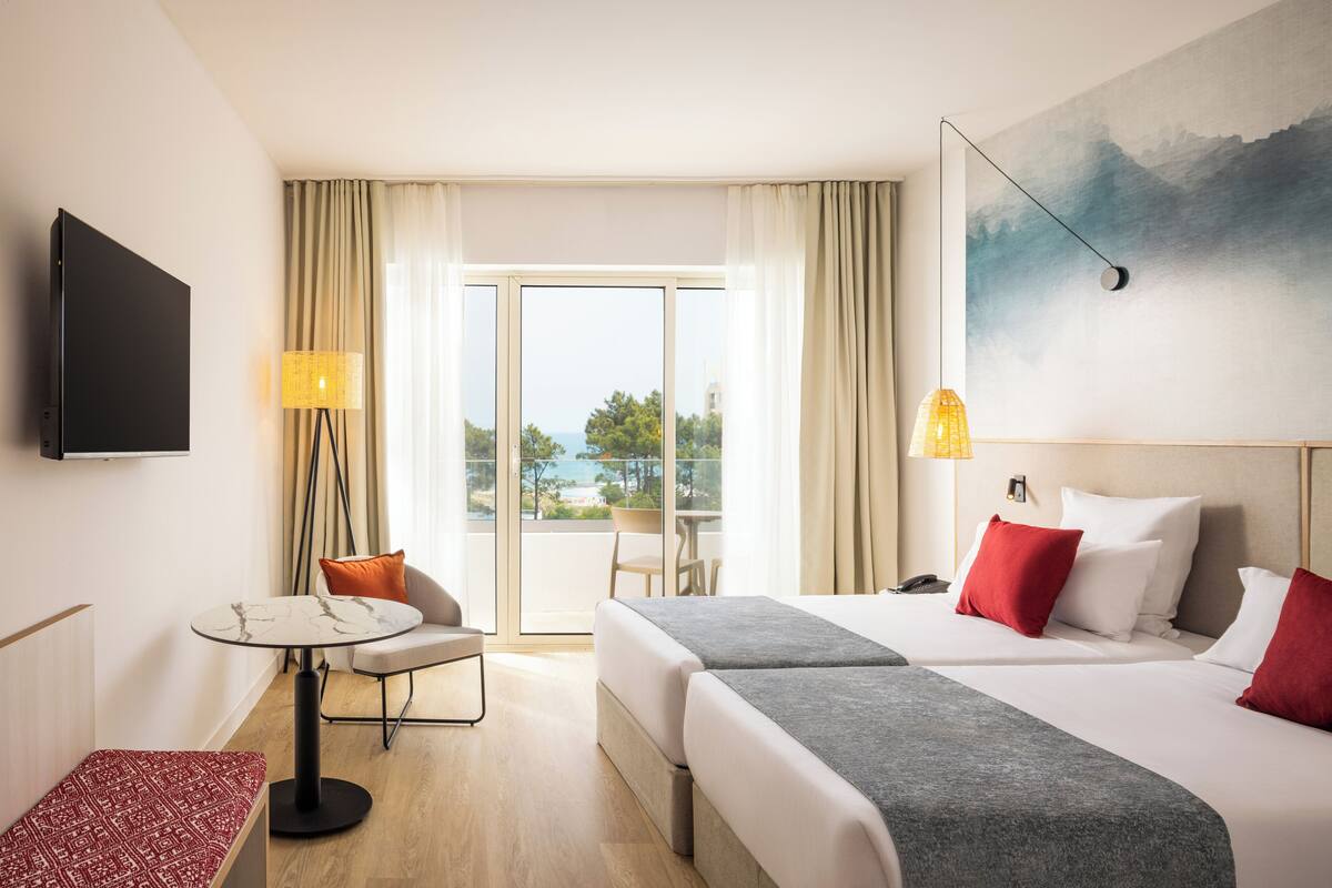 A hotel room with a bed, a desk, a chair, a TV, and a painting on the wall.