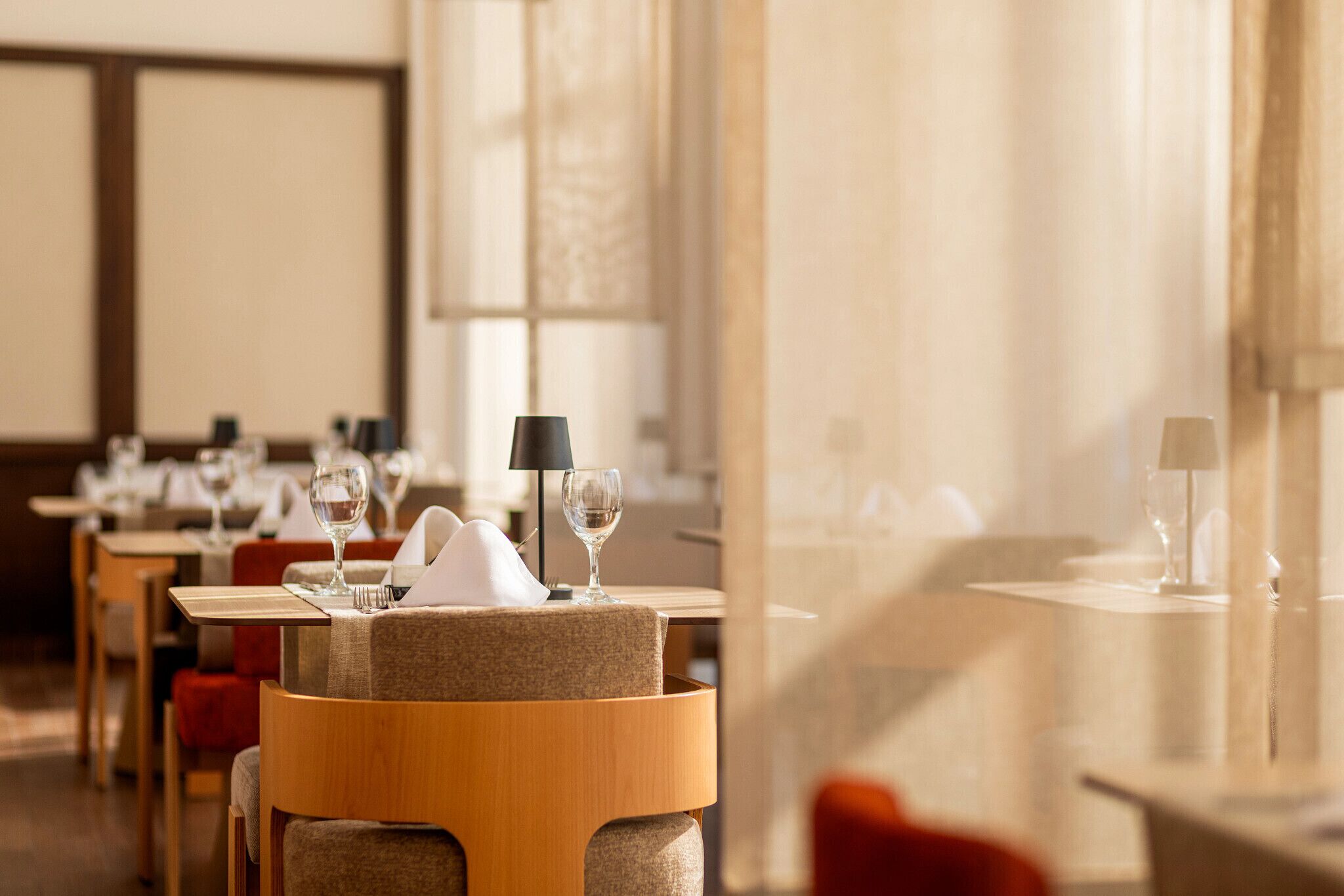 A restaurant with tables set for dining, featuring a modern design with wooden chairs and a neutral color palette.