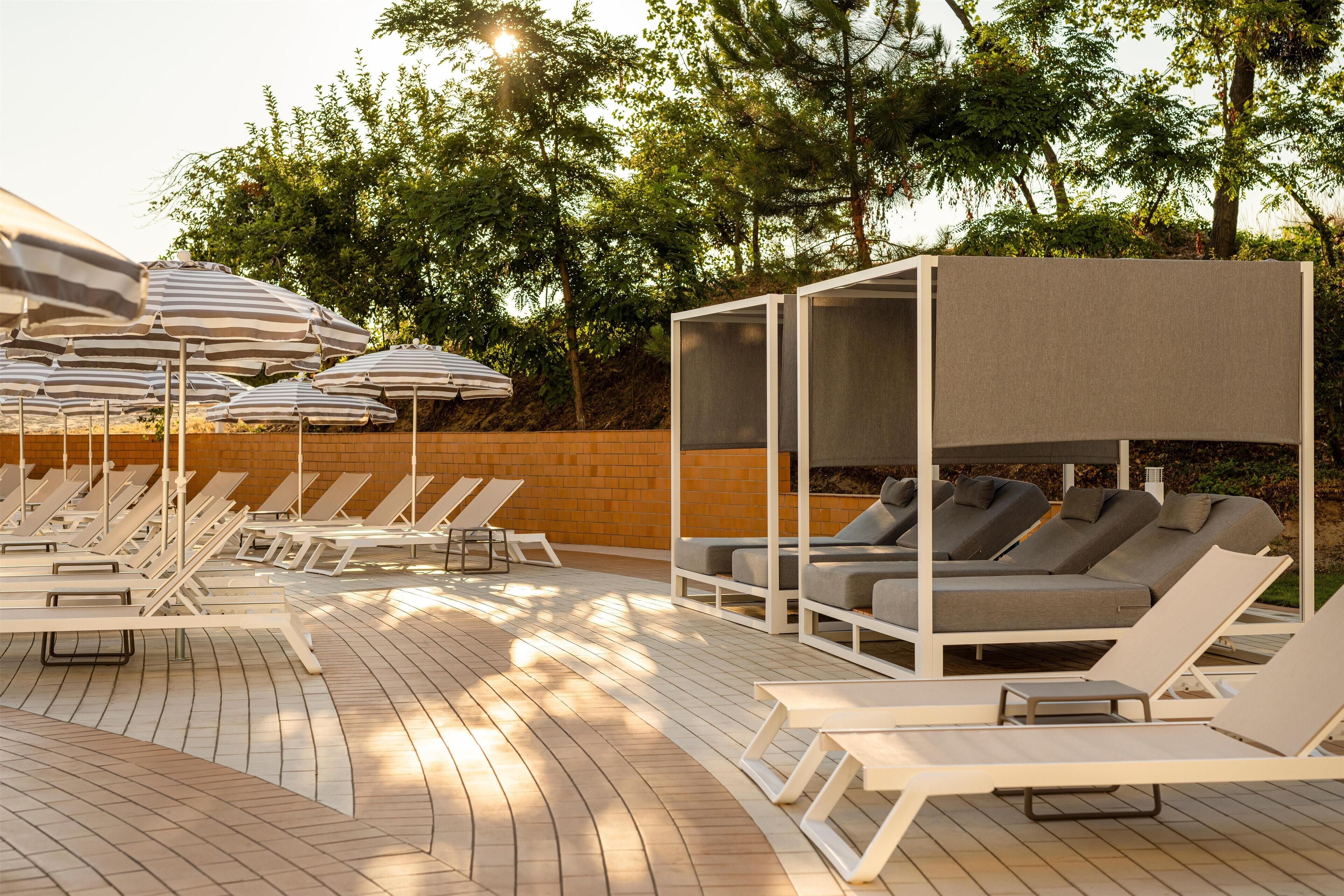 A poolside area with sun loungers, umbrellas, and a seating area with cushions.