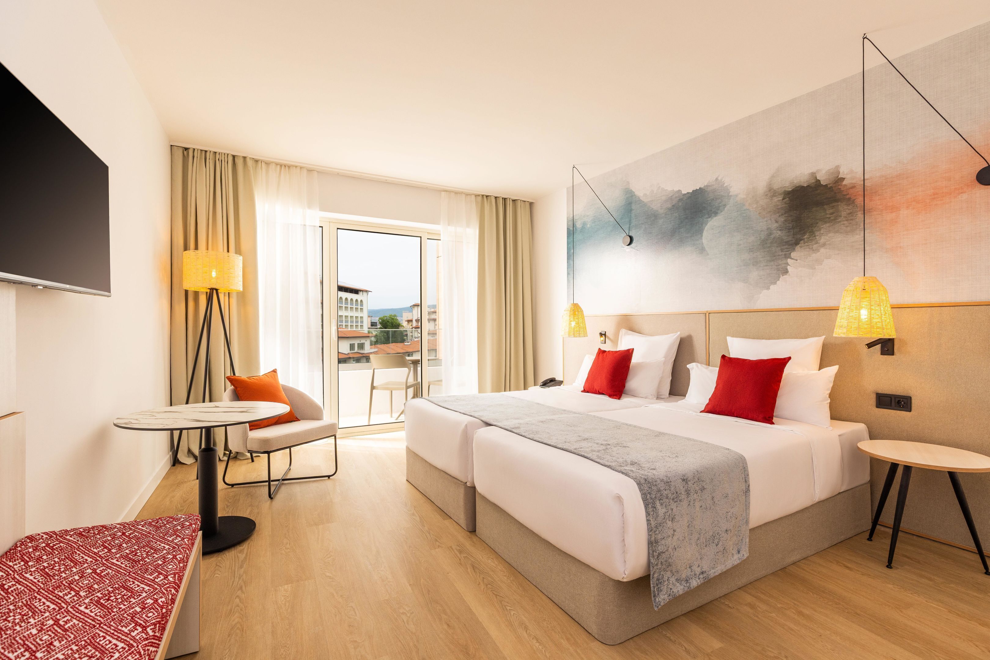 A hotel room with a bed, a desk, a chair, a TV, and a painting on the wall.