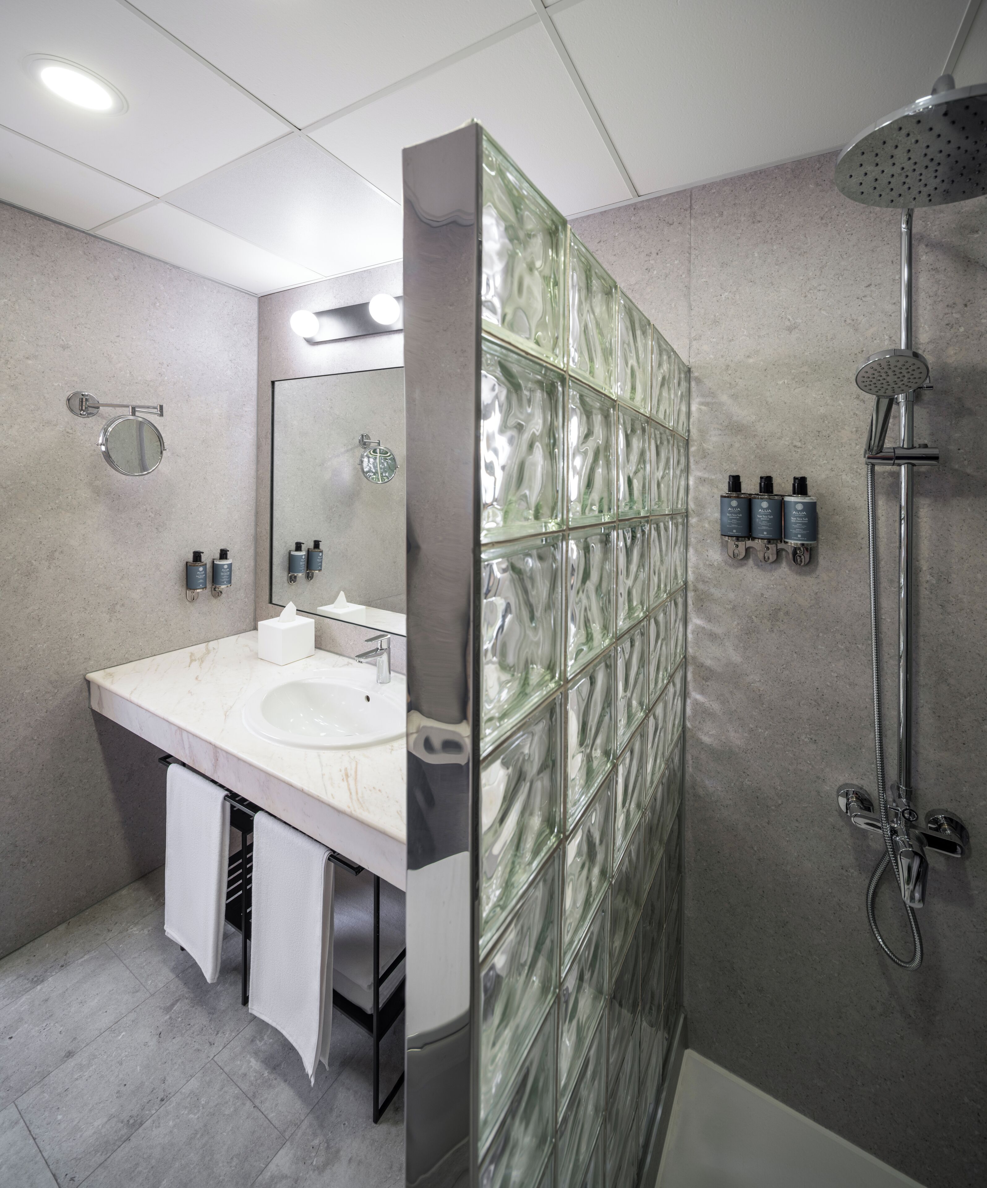 A modern bathroom with a glass shower enclosure, a round mirror, a white sink, and two towel racks.