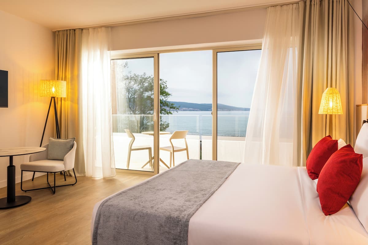 A hotel room with a bed, a table, chairs, and a balcony with a view of the sea.