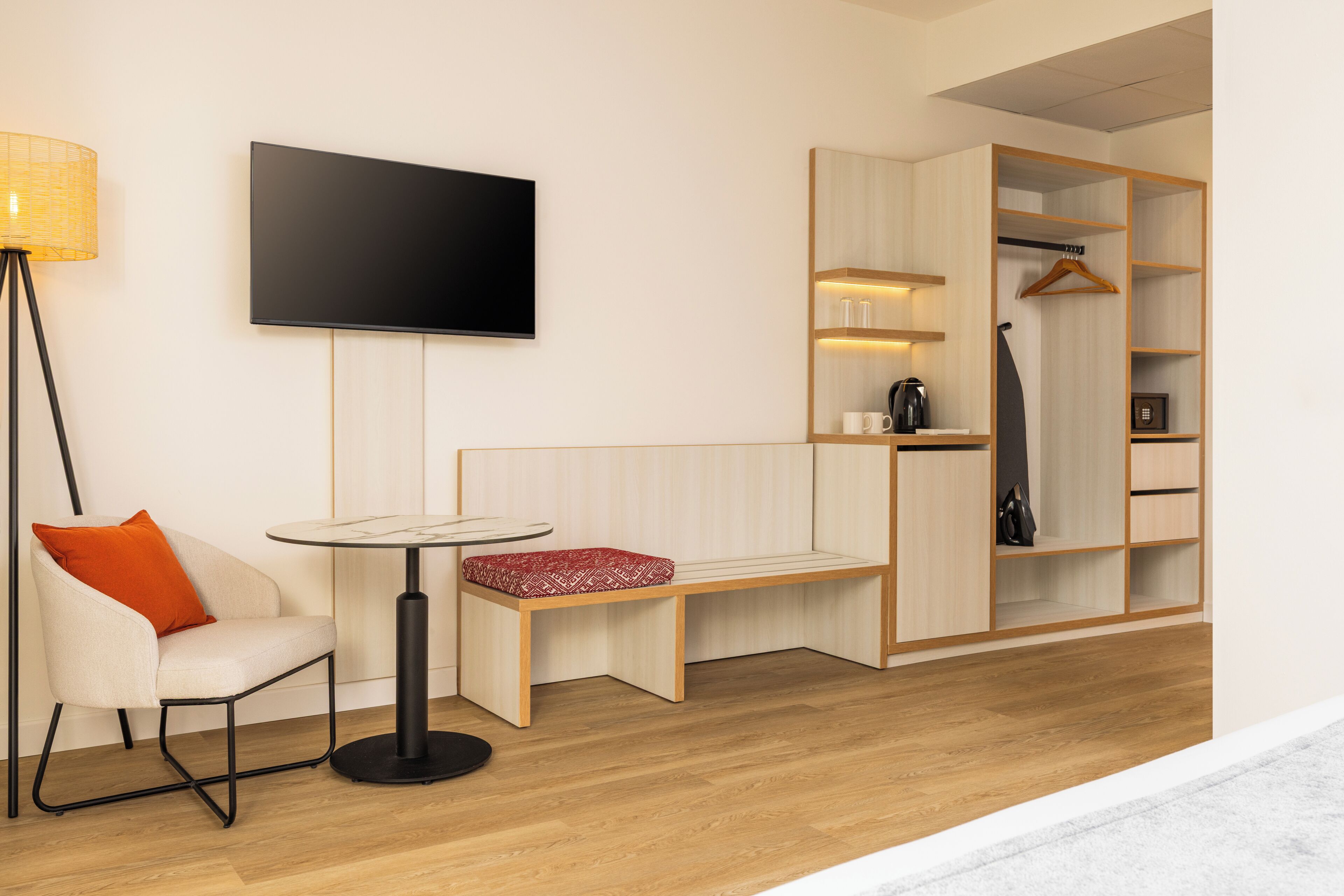 Une chambre moderne équipée d’un téléviseur à écran plat, d’une table ronde avec un banc, d’une chaise, d’une armoire et d’un lampadaire.