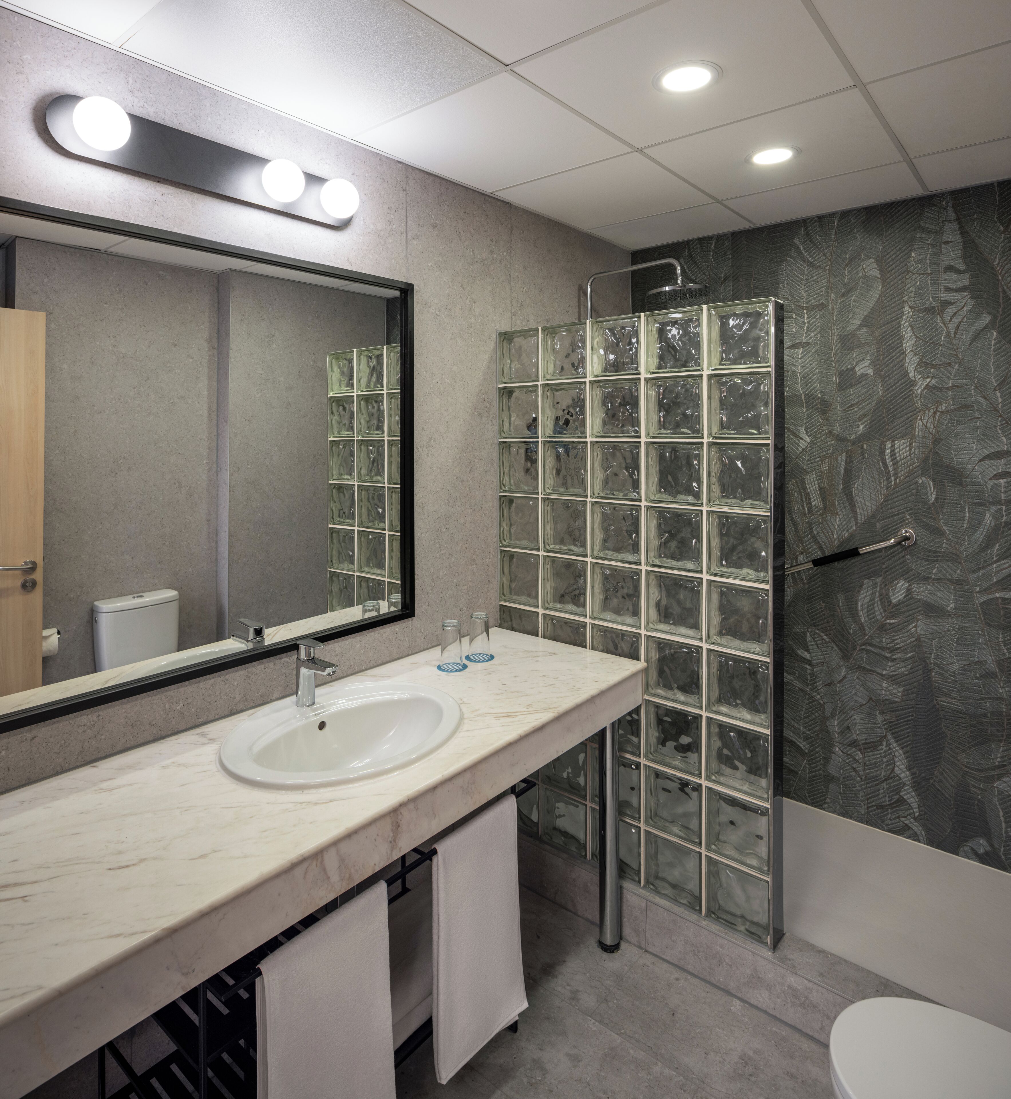 A bathroom with a marble sink, a large mirror, a glass shower enclosure, and a toilet.