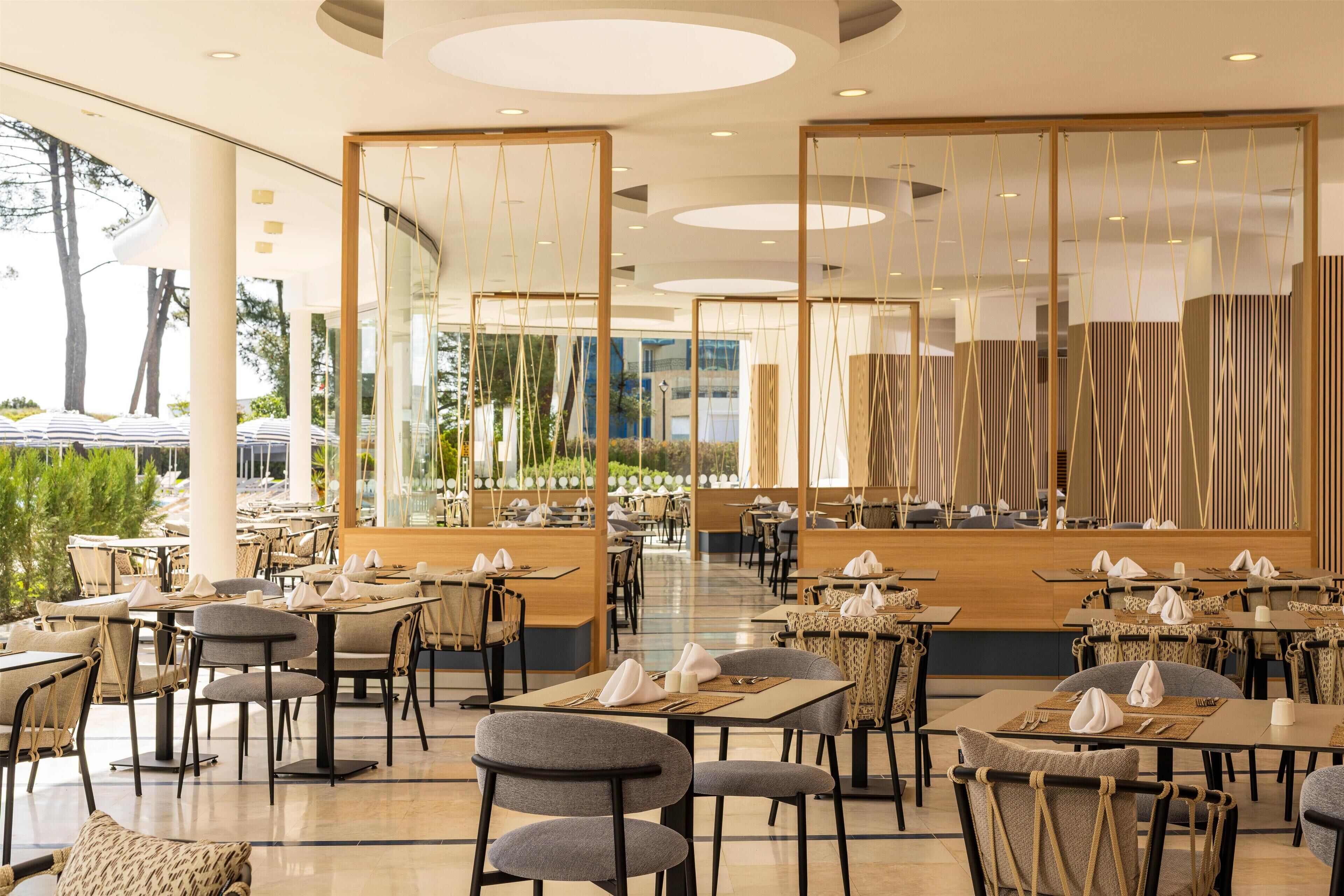 A spacious restaurant with multiple tables and chairs, large windows, and a modern interior design.