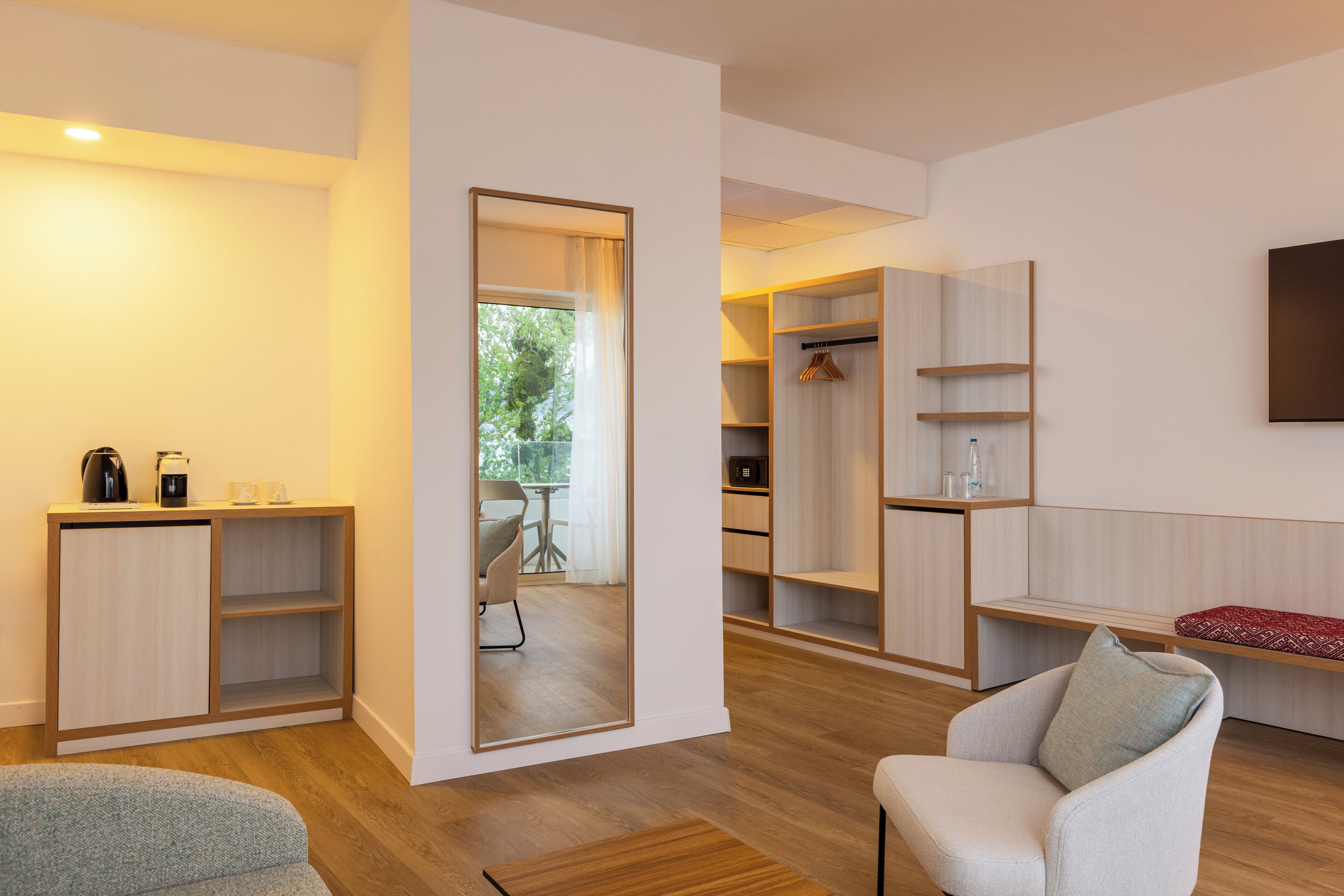 Una habitación moderna con suelo de madera, un sofá, una silla, una mesita de café, un espejo y un armario.