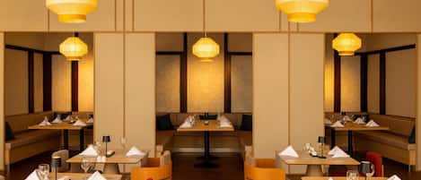 A restaurant with multiple tables and booths, each with a set table and a hanging light fixture.