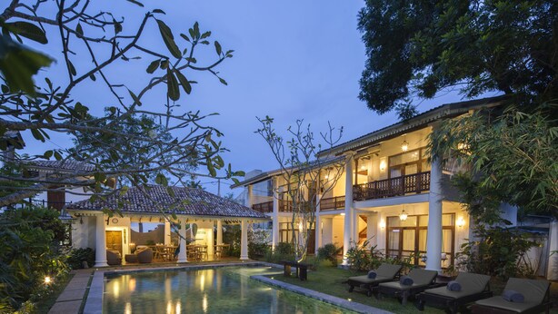 A two-story building with a swimming pool, outdoor seating, and a covered patio area. - Bilin Tree House (Galle)