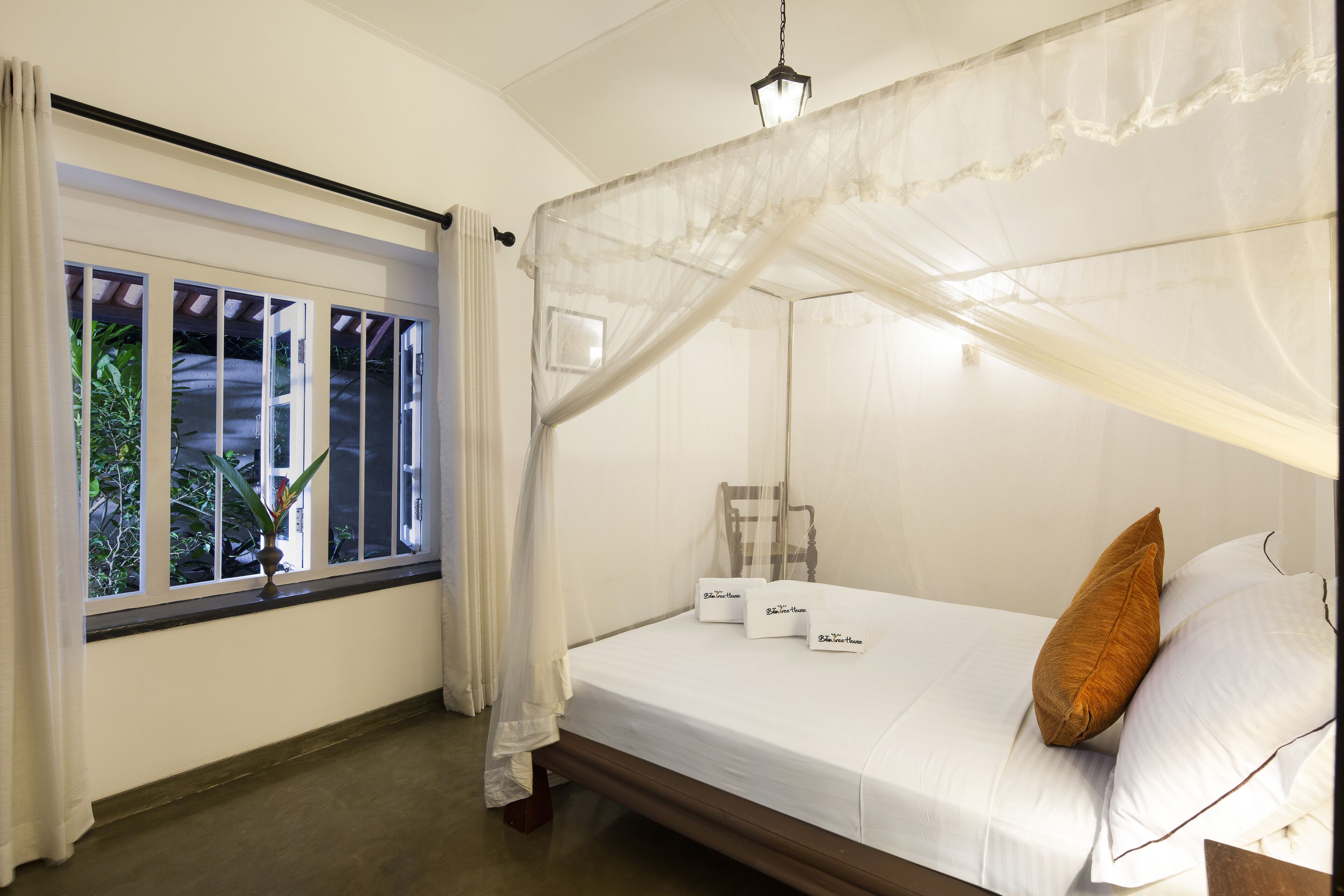 Una cama individual con dosel, una mesita de noche y una ventana con cortinas.