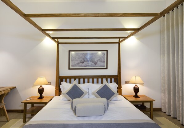 Habitación de hotel con techo de madera, una cama con ropa de cama blanca y dos almohadas, dos mesitas de noche con lámparas y un cuadro enmarcado en la pared.