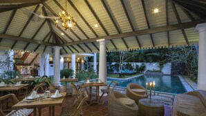An outdoor dining area with wooden tables and chairs, a pool, and a covered patio with a view of the pool. - Bilin Tree House (Galle)