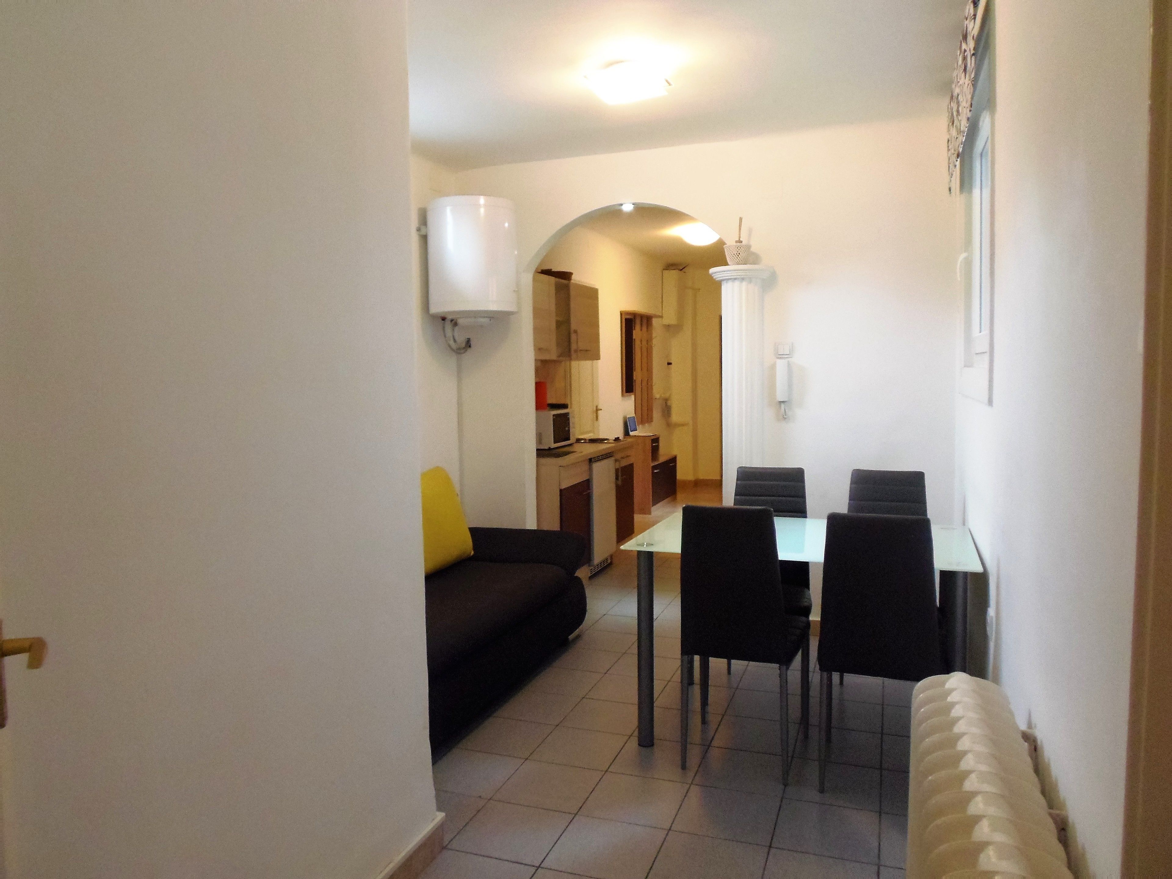 A compact living space with a dining area, a kitchenette, and a sofa with a yellow cushion.
