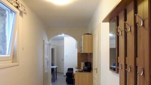 A narrow hallway with a window on the left, a door with a handle on the right, and a small wooden bench in the center.