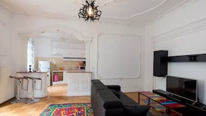 A modern living room with a black sofa, a colorful rug, a TV, and a kitchen in the background.