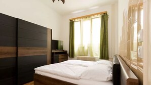 A bedroom with a bed, a wardrobe, a desk, and a window with curtains.