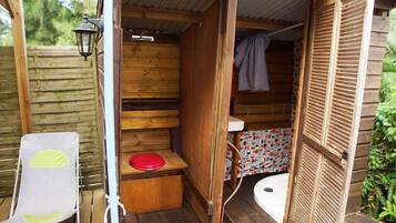 A wooden cabin with a small bathroom, a red toilet seat, and a shower area.