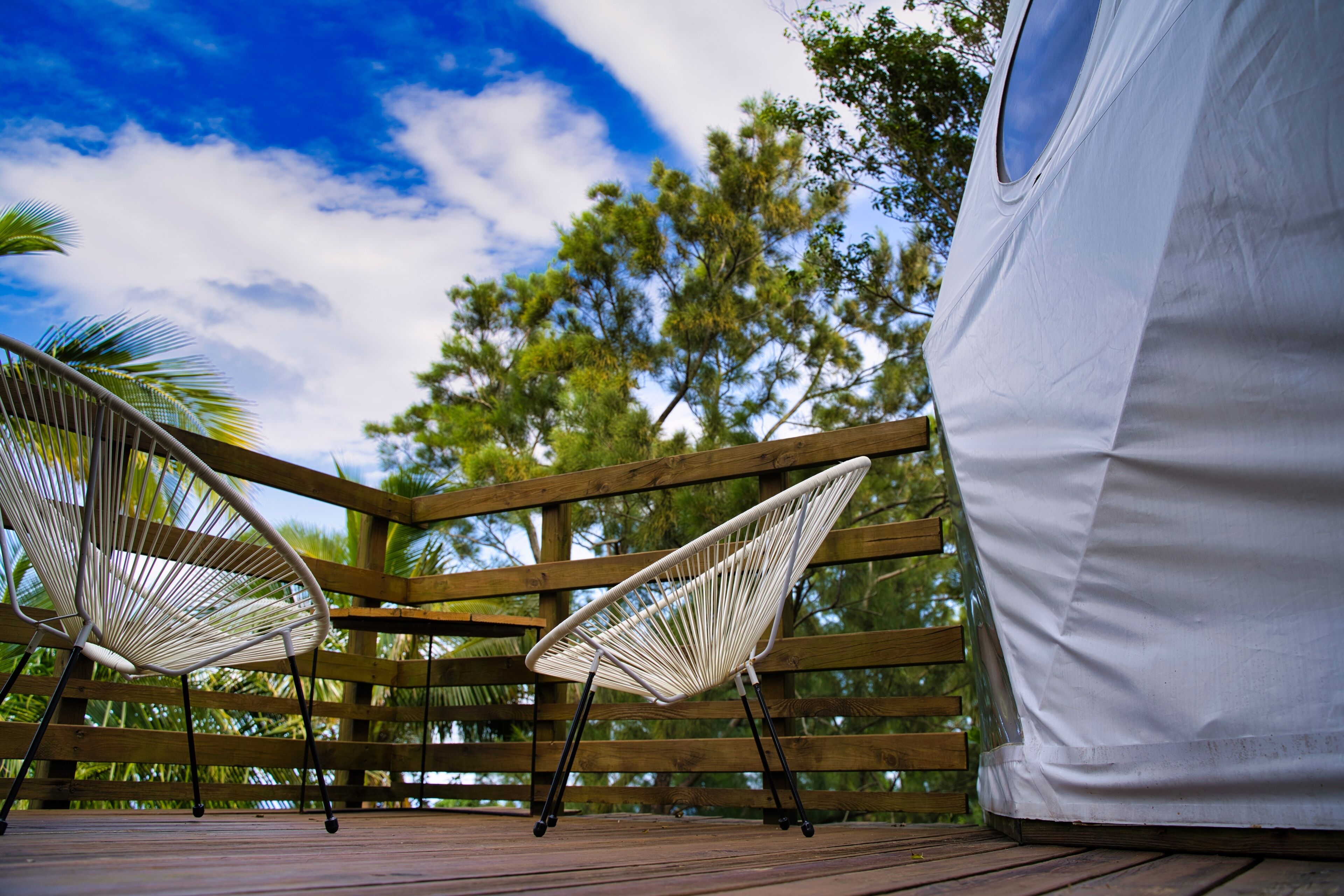 Una terraza de madera con dos sillas blancas de alambre y una carpa blanca.