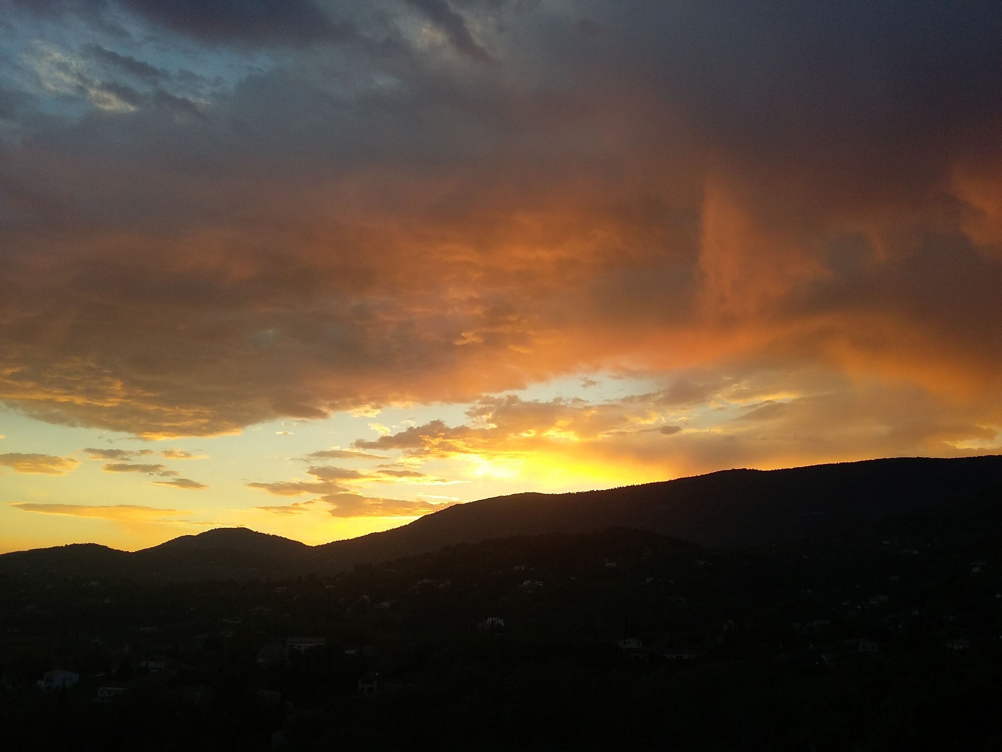 Ein Sonnenuntergang über einer gebirgigen Landschaft, im Tal sind Gebäude sichtbar.