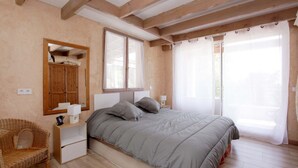 A bedroom with a bed, a nightstand, a chair, a wardrobe, and a window with curtains. - Large Provencal house with magnificent views in the heart of a historic village (Fayence)