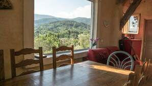 A dining area with a table and chairs, a red sofa, and a view of a mountainous landscape through a large window. - Large Provencal house with magnificent views in the heart of a historic village (Fayence)