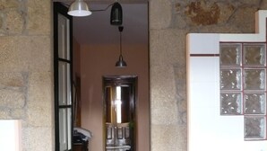 Een gang met een stenen muur, een betegelde vloer, een deur die naar een andere kamer leidt en een hangende lamp.