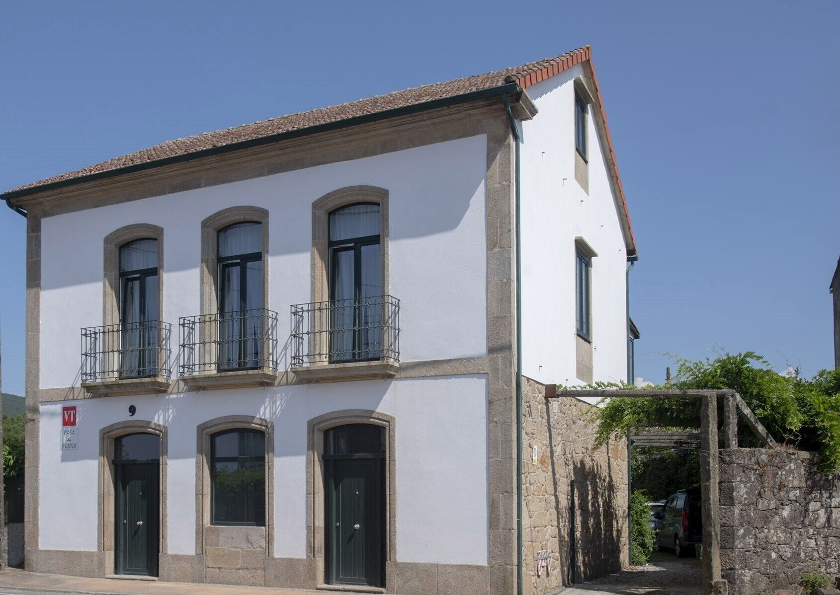 Un bâtiment à deux étages, doté d’une façade blanche, de trois fenêtres au rez-de-chaussée et d’un balcon avec des balustrades en métal.