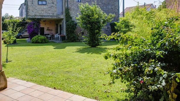 Een stenen gebouw met een tuin ervoor, een betegeld terras, en een metalen paal met een hangslot.