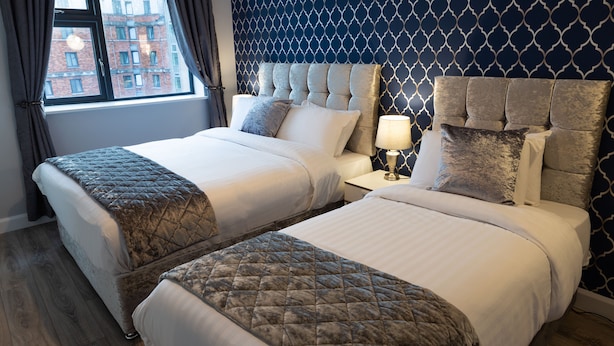 Une chambre d’hôtel avec deux lits, une table de chevet et une fenêtre avec des rideaux.