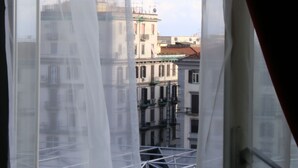 A view through a window with sheer curtains, revealing a building with multiple floors and balconies. - B&B Re Ferdinando (Naples)