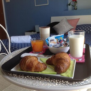 Bandeja de desayuno con cruasanes, jugo, leche y cereales sobre una mesa en una habitación de hotel.
