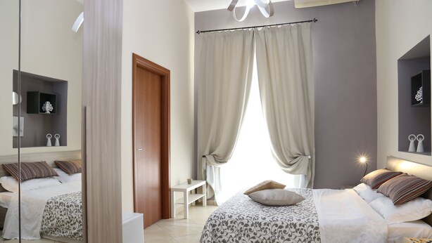 A bedroom with two beds, a bedside table, a mirror, and a window with curtains. - B&B Re Ferdinando (Naples)