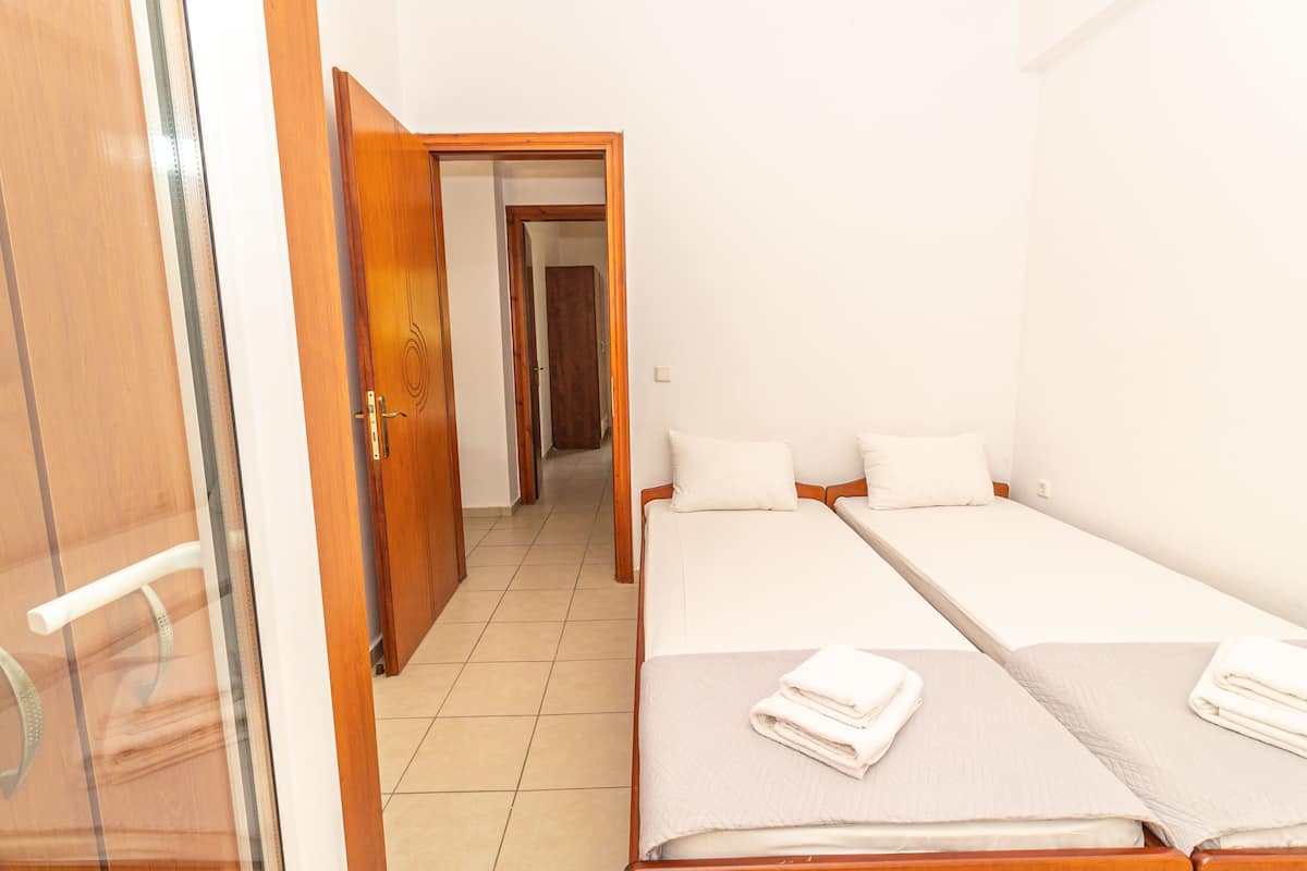 A hotel room with two single beds, a wooden door, and a tiled floor.