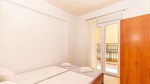 A small, clean room with two single beds, a wooden door, and a balcony with a railing. - Sunday Mood (Kassandra)