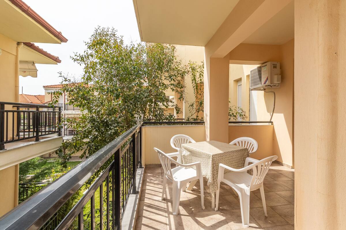 A balcony with a table and chairs, an air conditioning unit, and a view of a garden.
