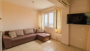 A living room with a brown sofa, a flat-screen TV, a window with curtains, and an air conditioning unit. - Sunday Mood (Kassandra)