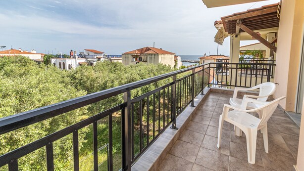 A balcony with a view of a coastal area, featuring a tiled floor and two white plastic chairs. - Sunday Mood (Kassandra)