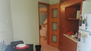 A compact kitchen with a dining table set for two, a refrigerator with magnets, and a small cabinet. - Salamina's Apartment (Salamis)