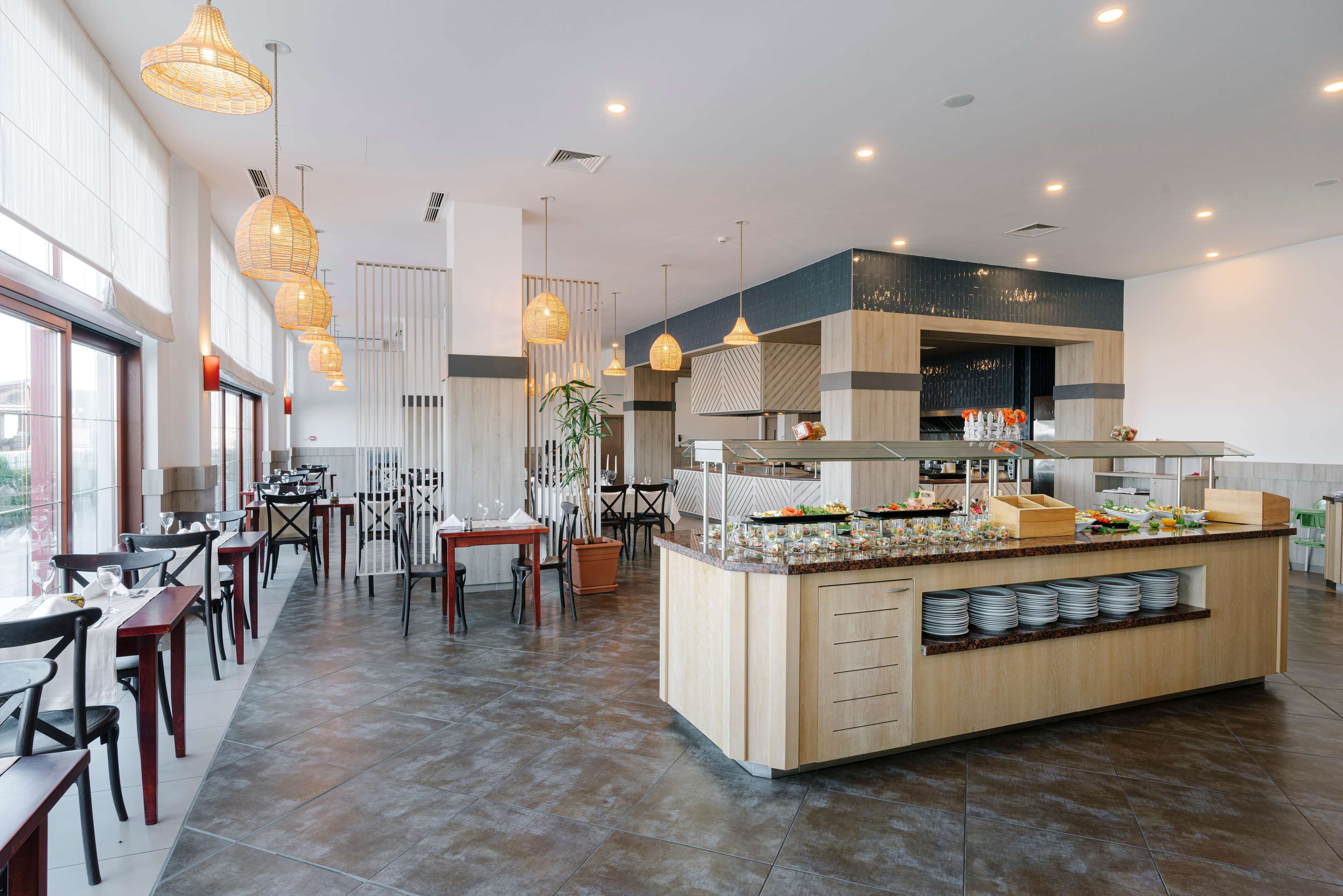 A modern restaurant with a central island, dining tables, and hanging pendant lights.