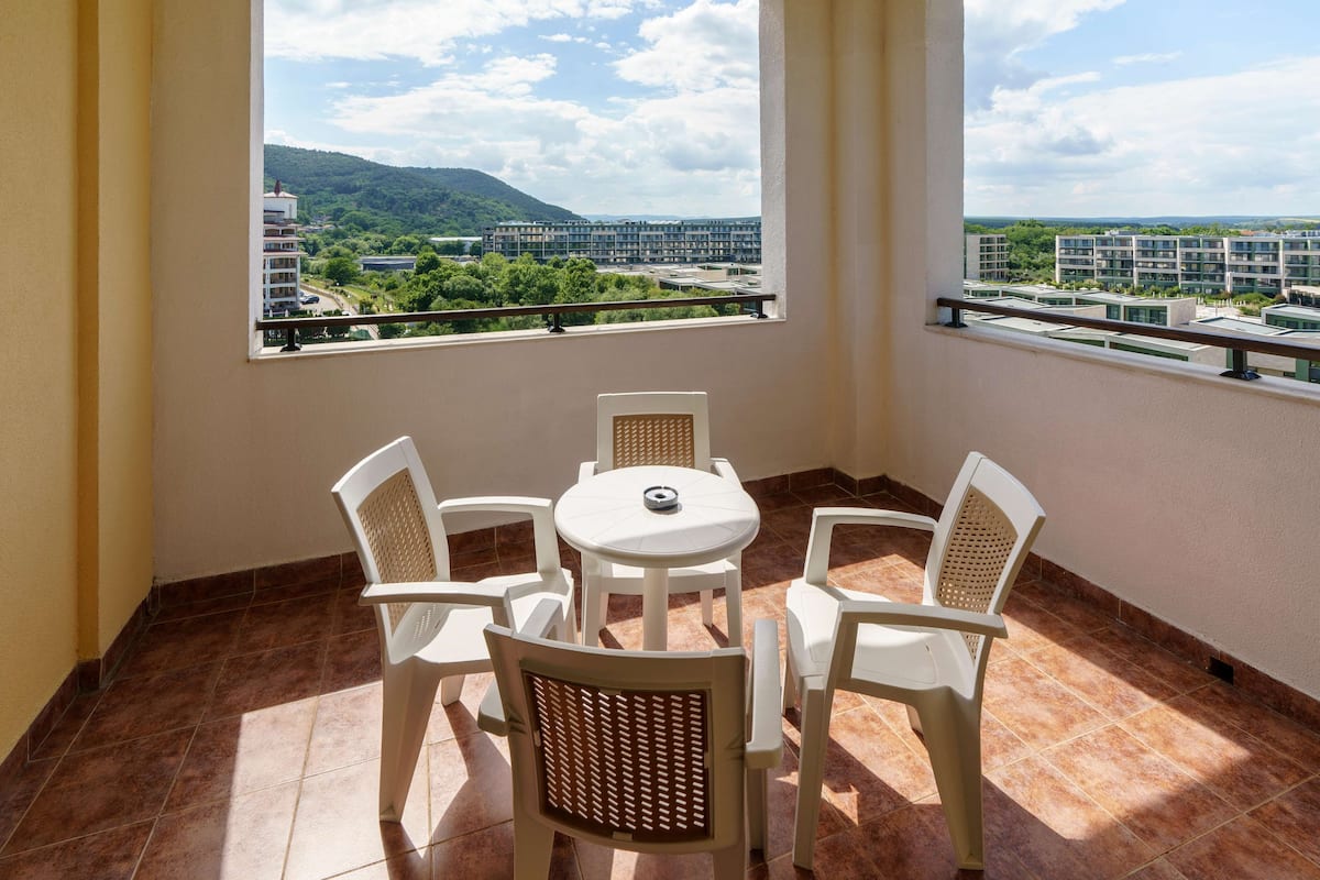 A balcony with a table and chairs, a view of buildings and greenery, and a tiled floor.