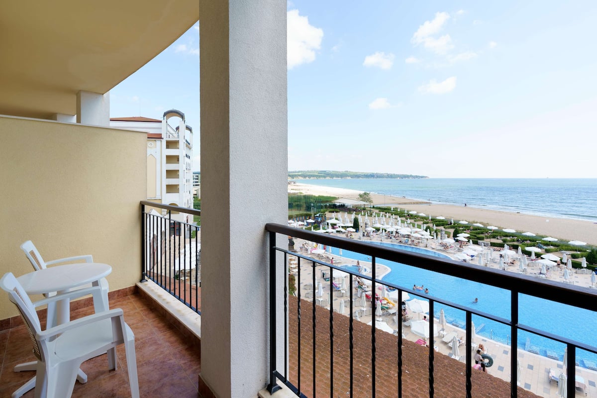 A balcony with a view of a beach and a pool area.